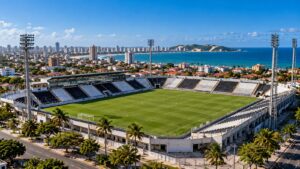 Estádio com cadeiras pretas e brancas e quatro torres de iluminação em bairro litorâneo de Natal