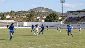 Partida de futebol feminino em estádio do Nordeste em tarde ensolarada