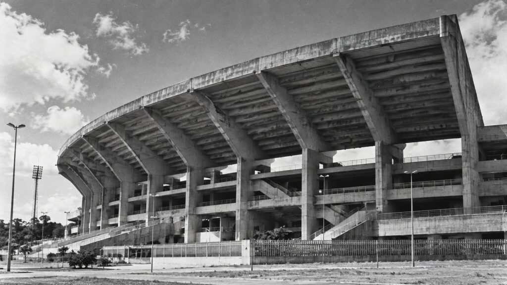 Estádio de concreto dos anos 1970 com marquise curva, em estilo de fotografia antiga