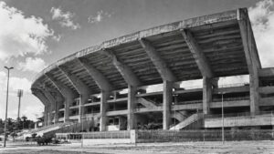 Estádio de concreto dos anos 1970 com marquise curva, em estilo de fotografia antiga